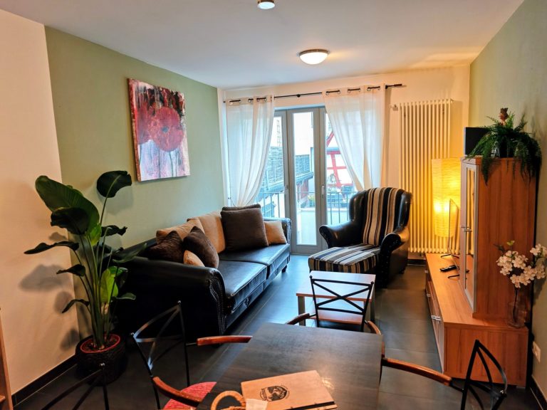 Living room of the ‘Rhein & Wein’ apartment in Bacharach, with sofa, armchair and French windows facing the historic old town.