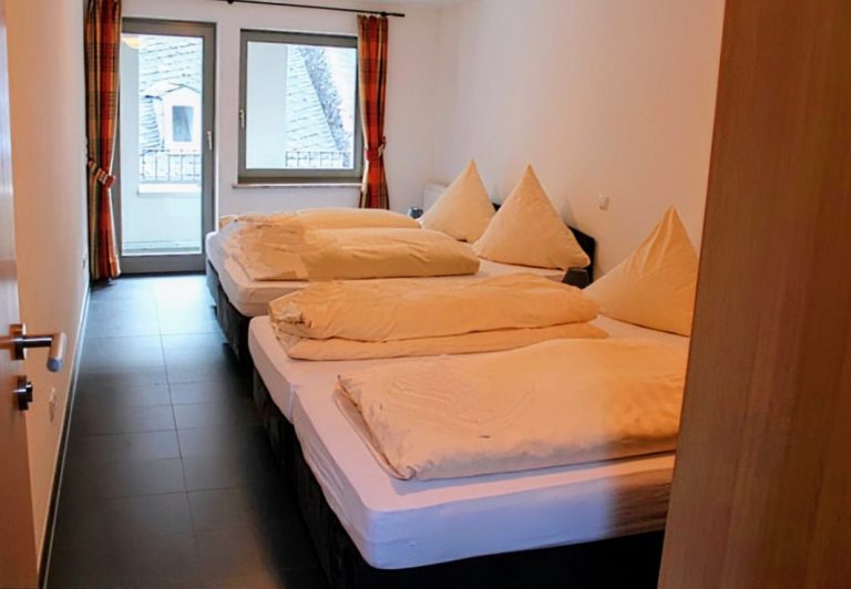 Schlafzimmer mit zwei Doppelbetten und Balkon mit Blick auf Burg Stahleck und Altstadt – Altstadtquartier 16